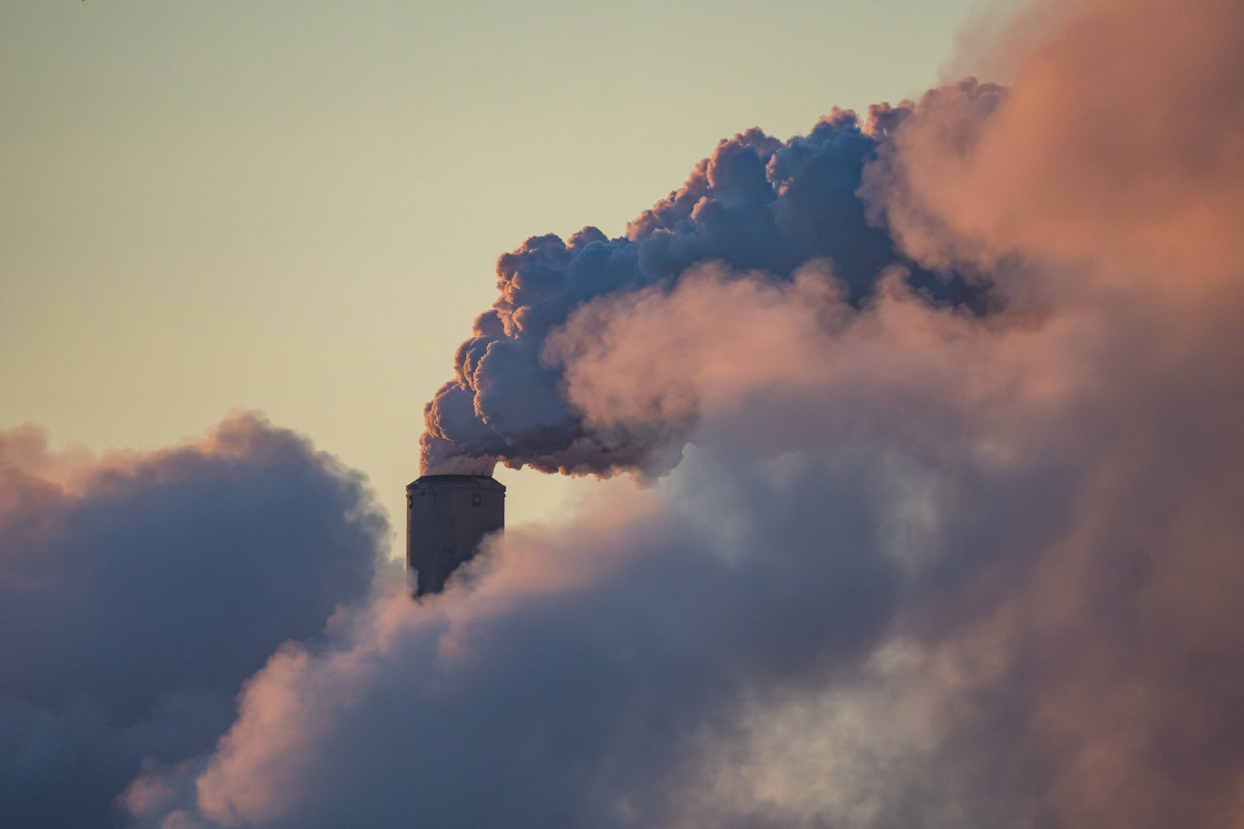 Close-up of pollution and steam rising out of the top of a smokestack against a yellow-ish sky.