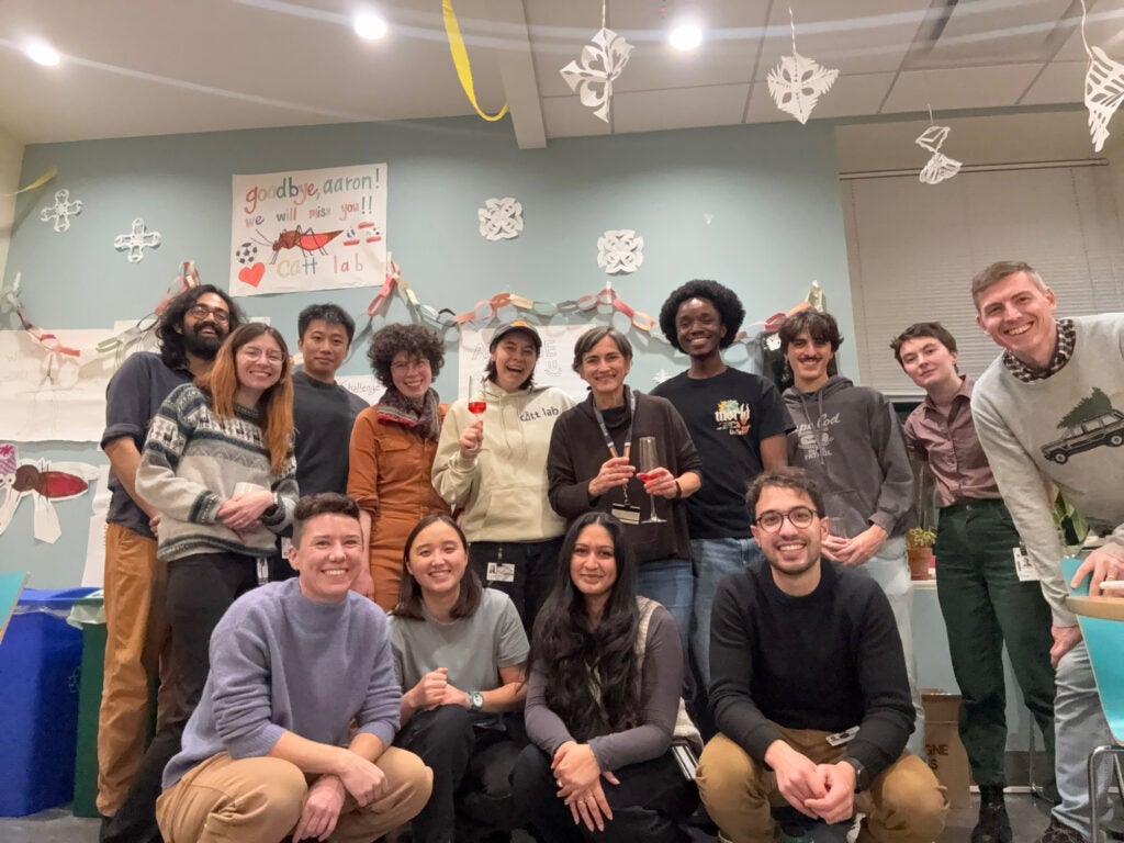 The Catteruccia Lab celebrating at one of their farewell parties with paper snowflakes hanging from the ceiling and a sign that says, "Goodbye, Aaron! We will miss you! Catt Lab."