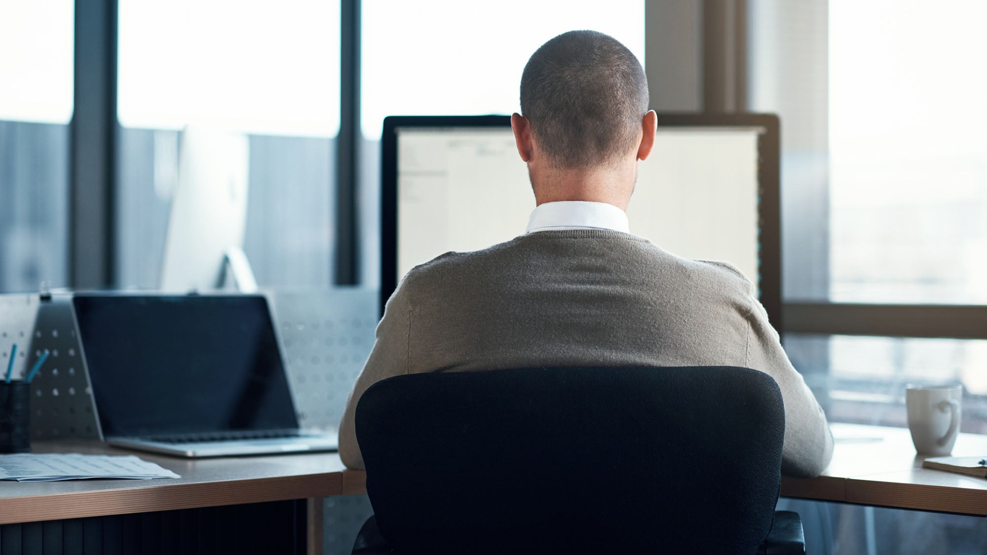 A man pictured from behind works in an office at a computer