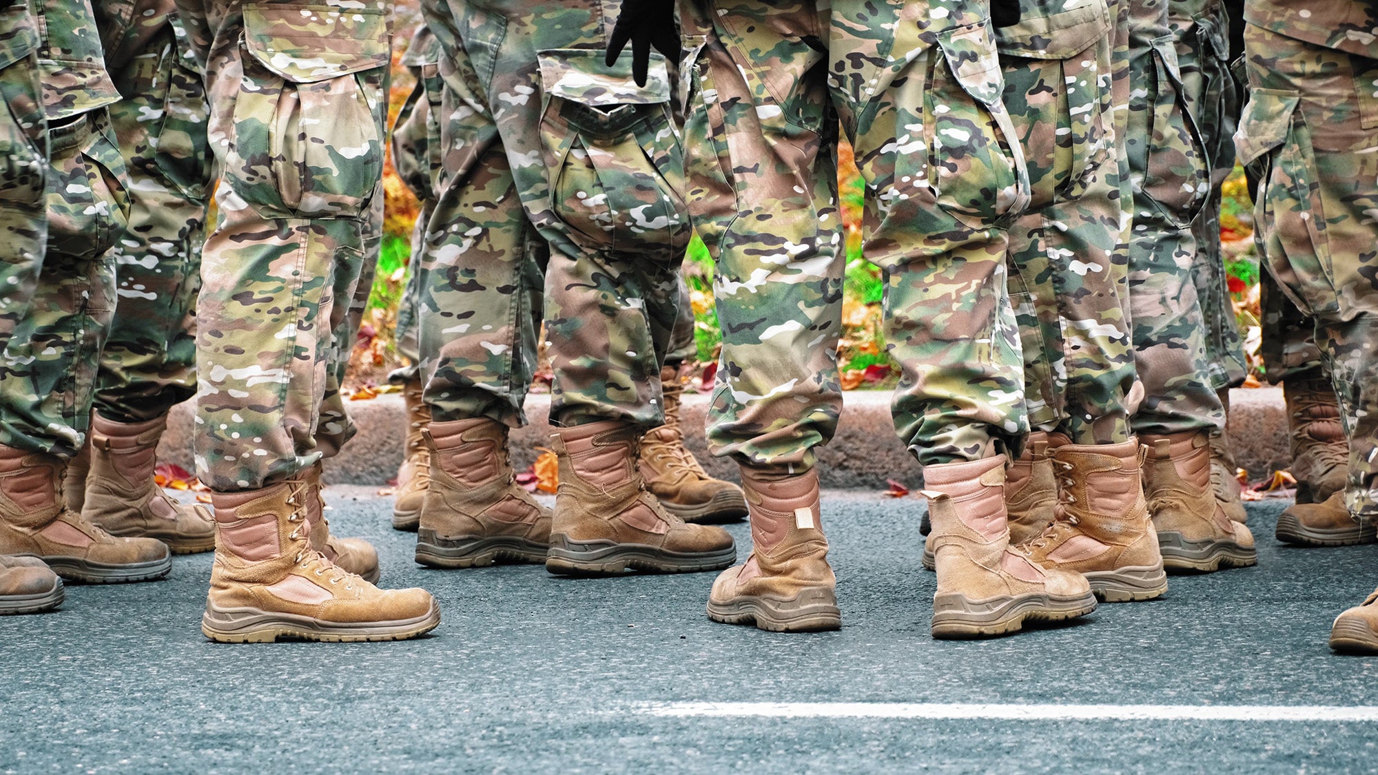 Group of soldiers wearing camouflage uniforms and tactical boots, standing on asphalt road