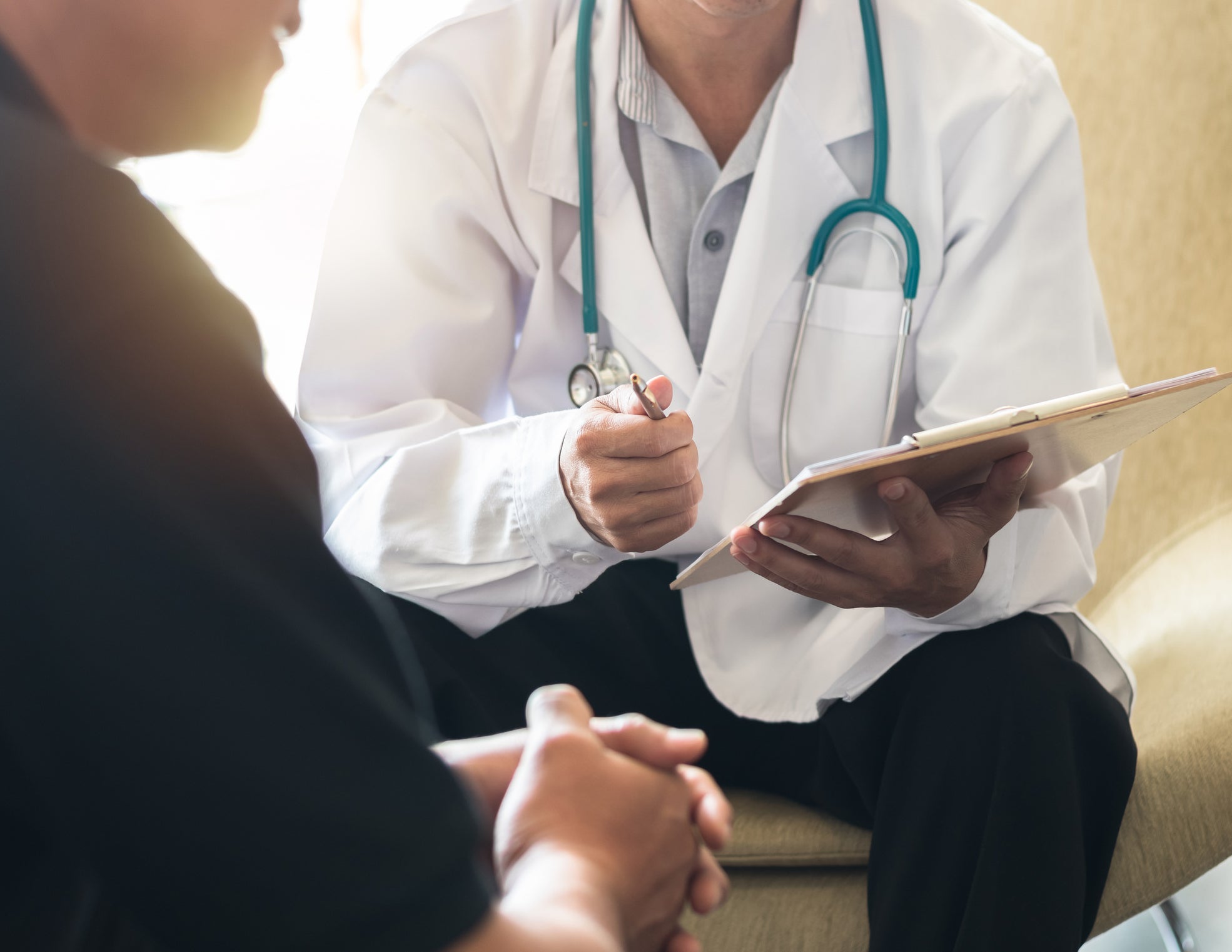 Close-up of male patient and physician having a discussion, zoomed in on their torsos and hands
