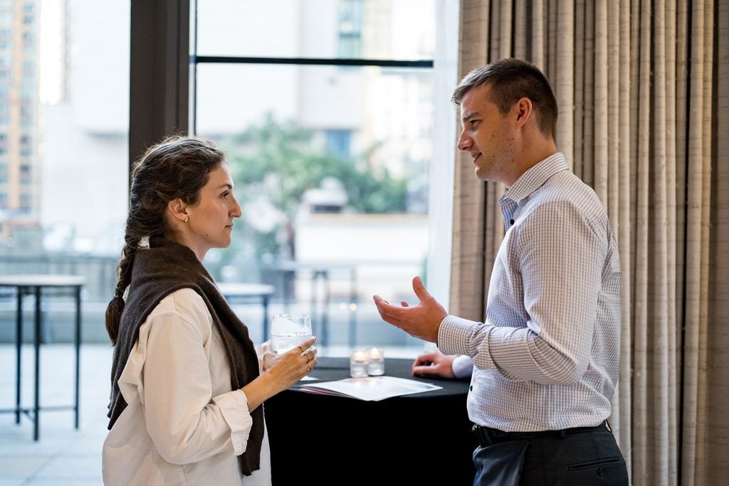 Two guests converse at a high-top table, one holding a glass. 