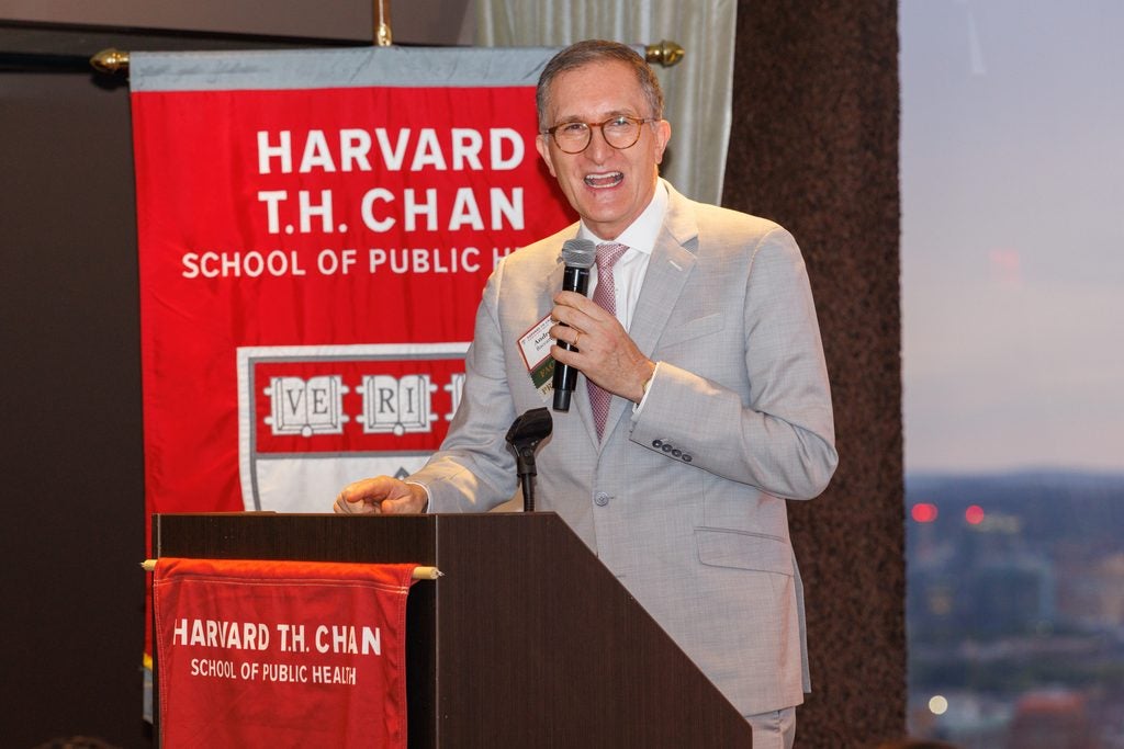 Dean Andrea Baccarelli smiles while speaking at the podium. 