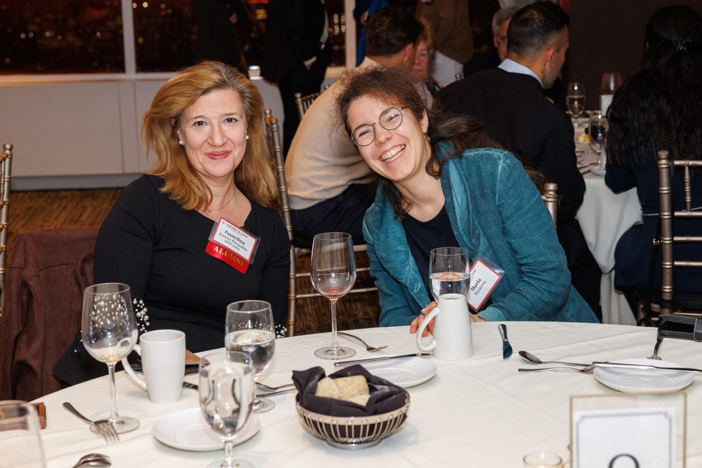 Two alumnae smiling, seated at a table. 
