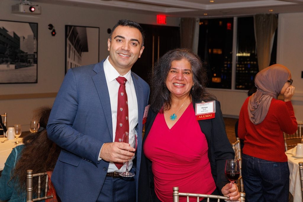 A man in a Harvard Chan School tie poses with a woman in a bright red shirt. 