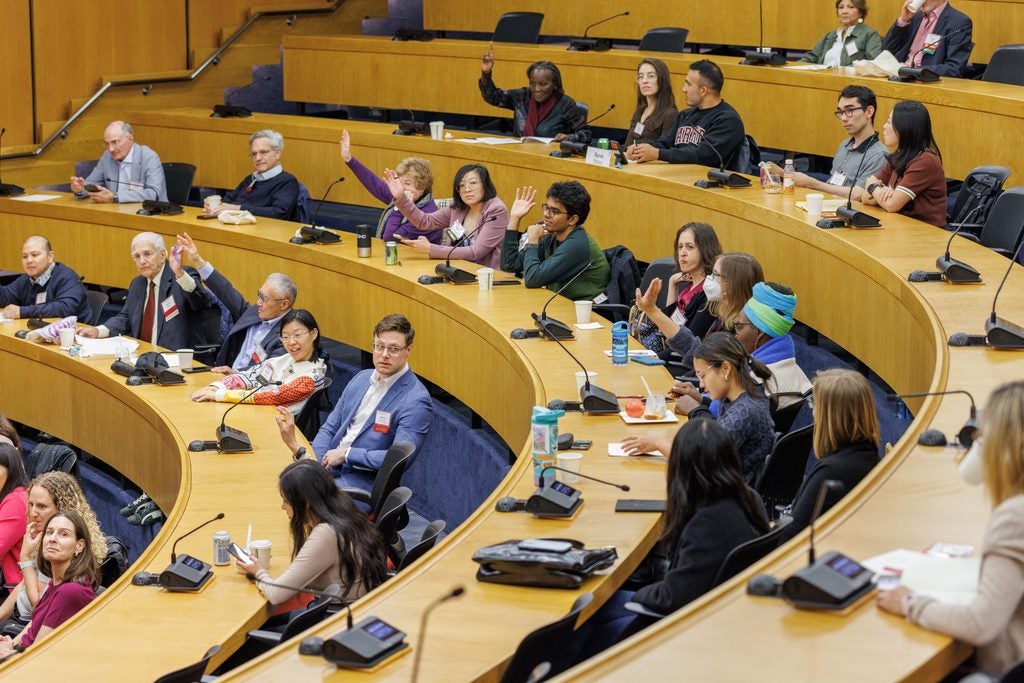 A wide view of the lecture hall showing engaged attendees, many with their hands up. 