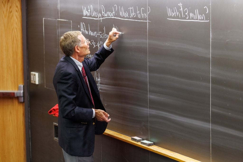 Rick Siegrist writes on the chalkboard, which has three headings: What Driving burnout, Whose job to fix,  and Worth $1.3 Million?