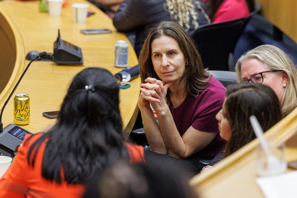 A woman interlaces her fingers while listening to conversation with three other seated women in the lecture hall. 