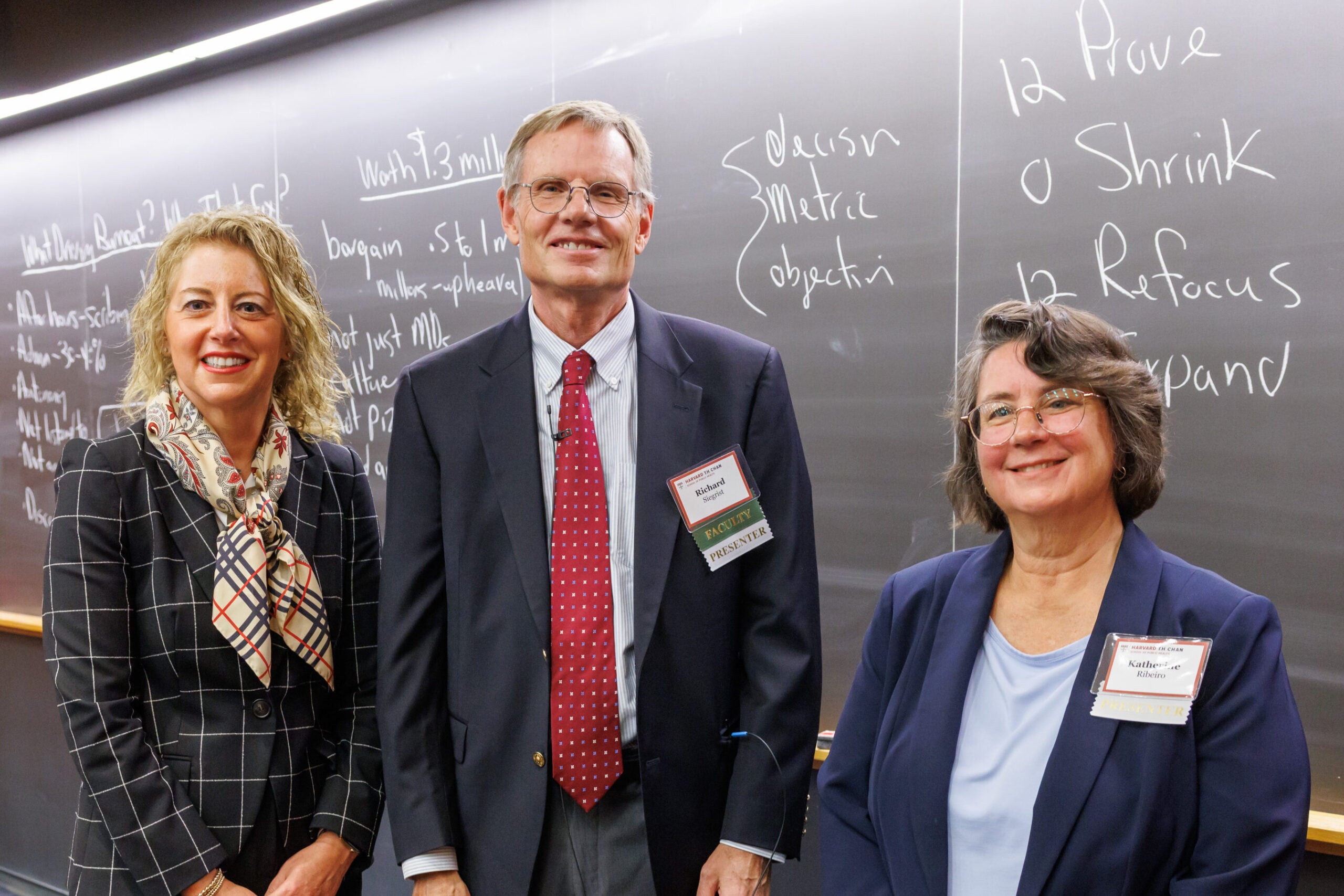 Rick Siegrist poses in front of the full chalkboard with two attendees. 