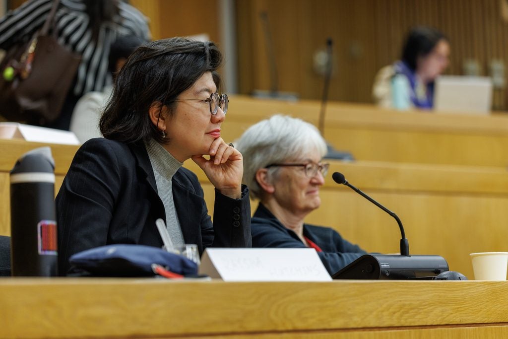 A woman listens with her hand on her chin, and Nancy Turnbull in the background. 