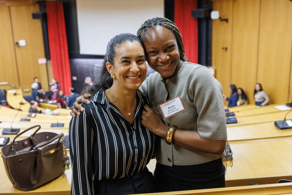 Two alumnae pose, embracing closely, in  the back of the lecture hall. 