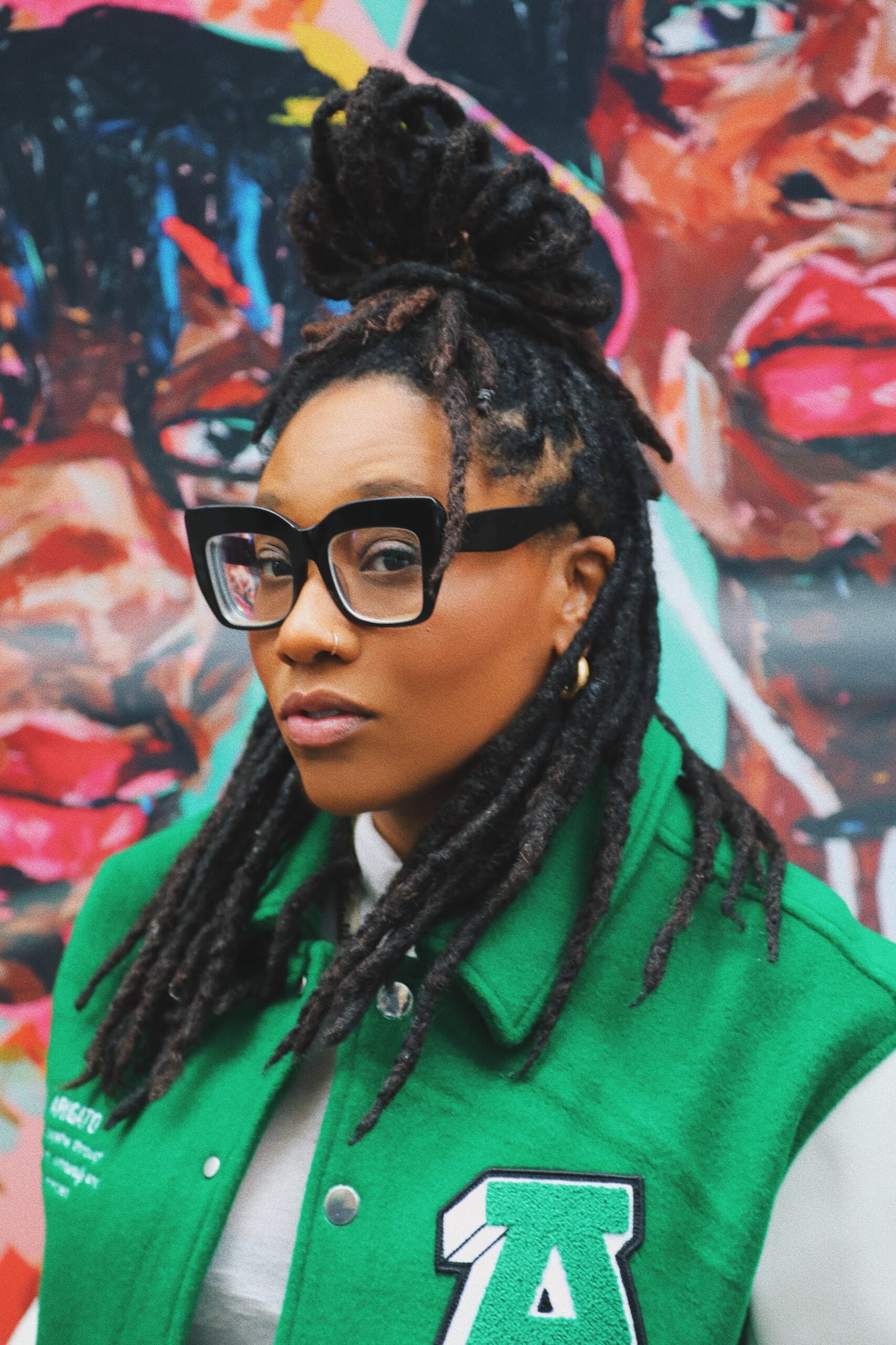Natalie Lauren Sims wearing a green letterman jacket and black glasses.