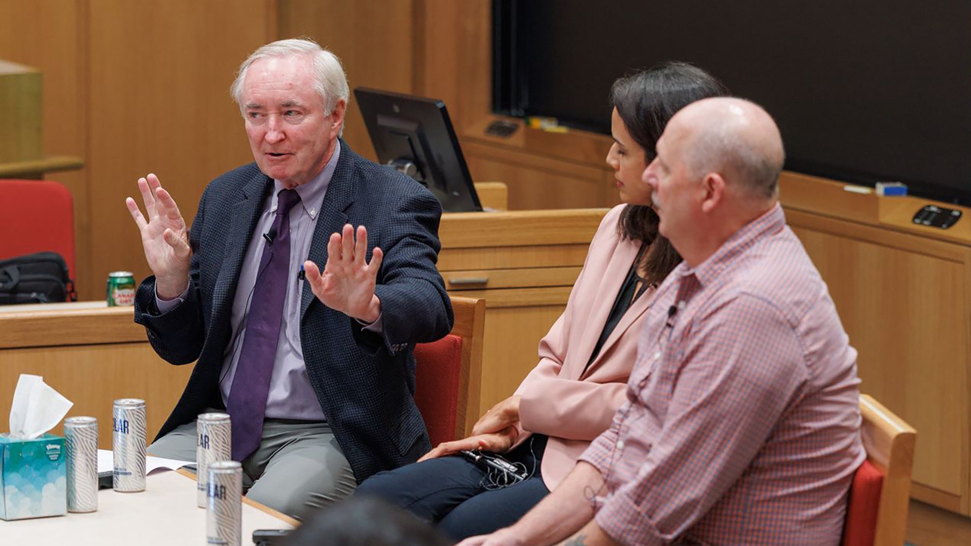 A man gestures while speaking as two other panelists listen.