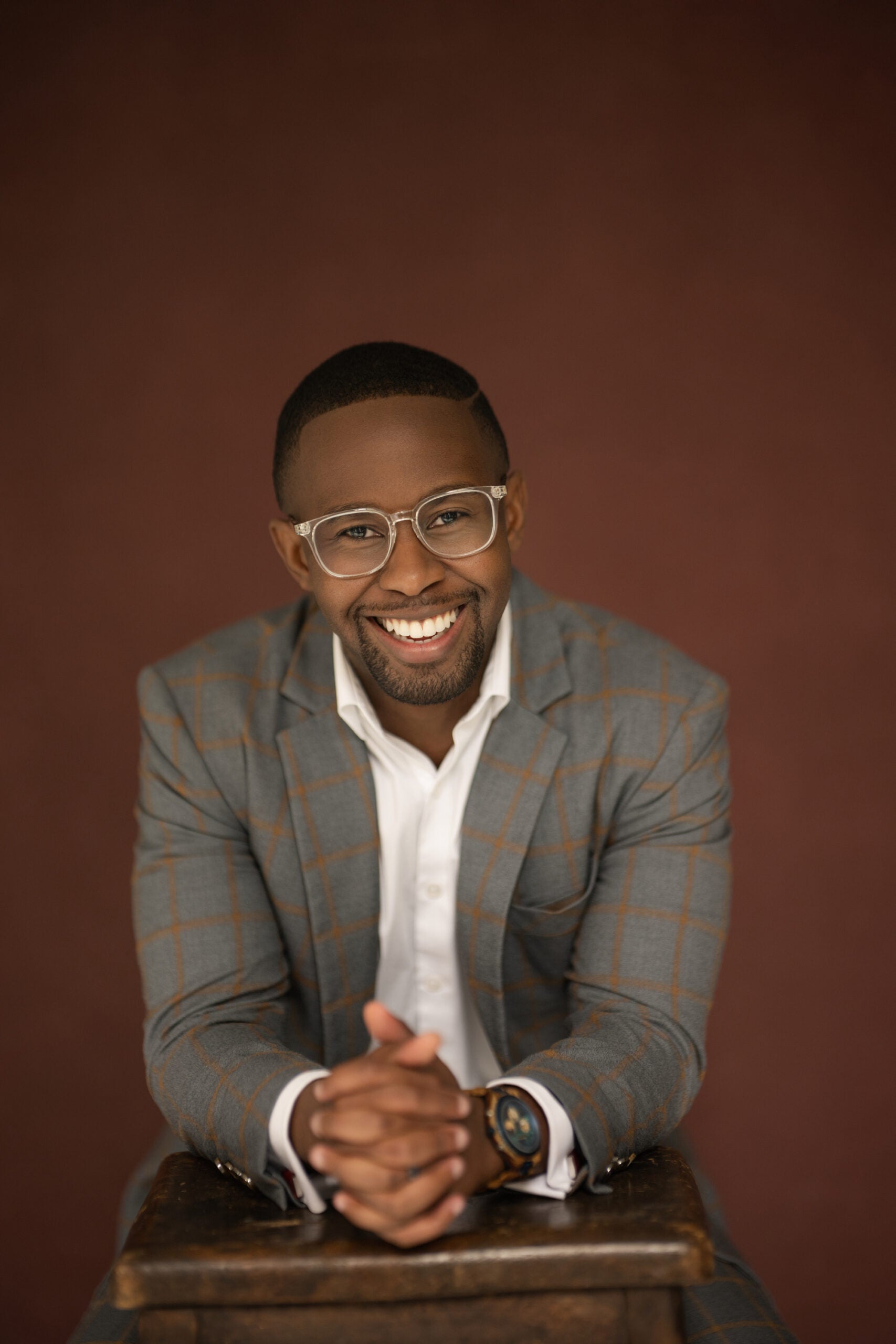 Dr. Michael Forde wearing a white button up shirt with a grey and brown checkered suit jacket against a warm brown backdrop