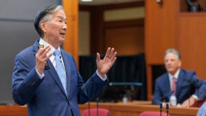 A man gestures while speaking as an audience member watches.
