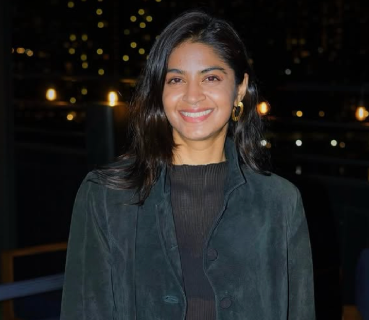 Dr. Varuna Srinivasan from the waist up wearing a dark blue jacket and grey shirt.
