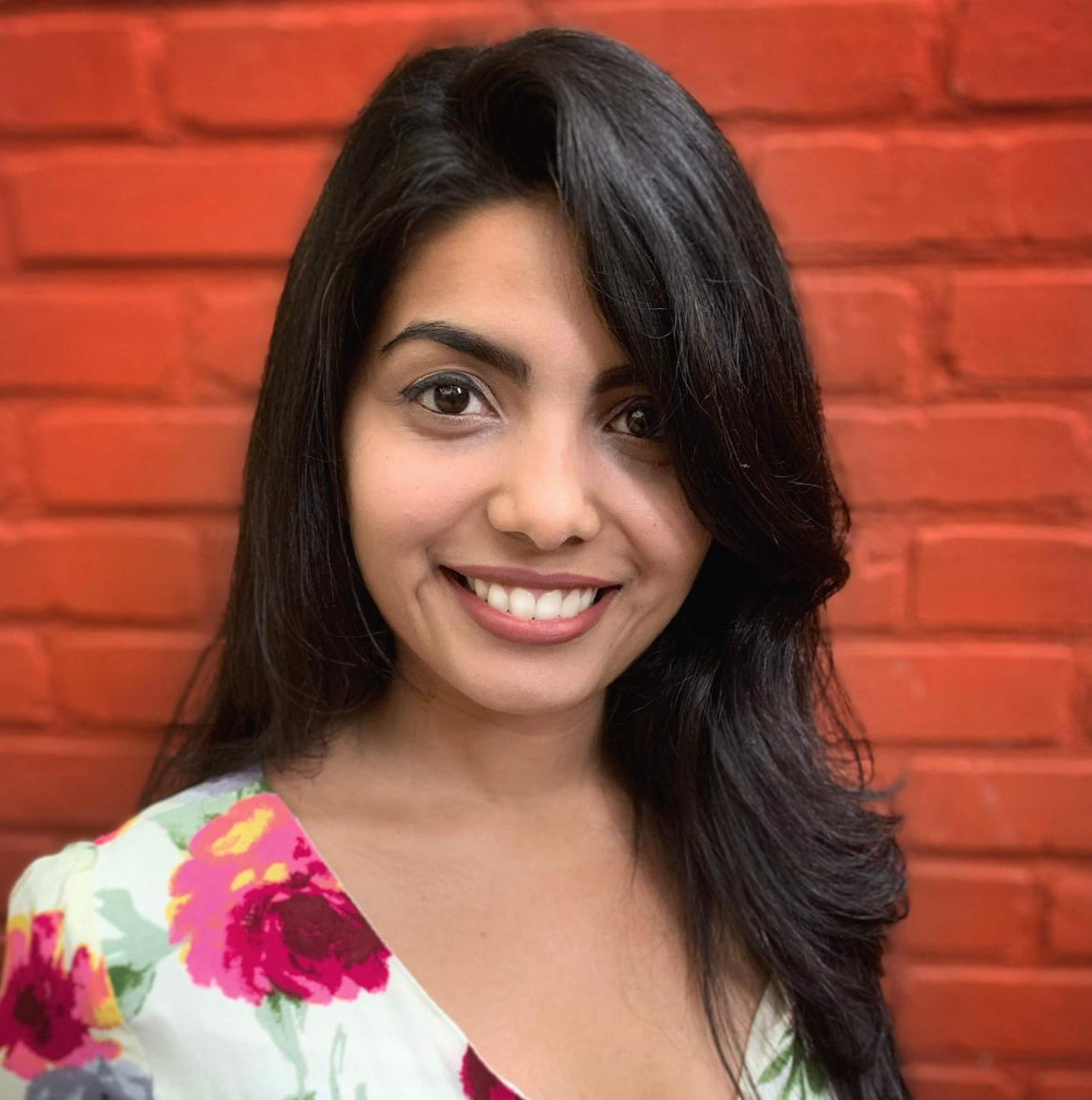 Pari is wearing a floral blouse against a red brick backdrop