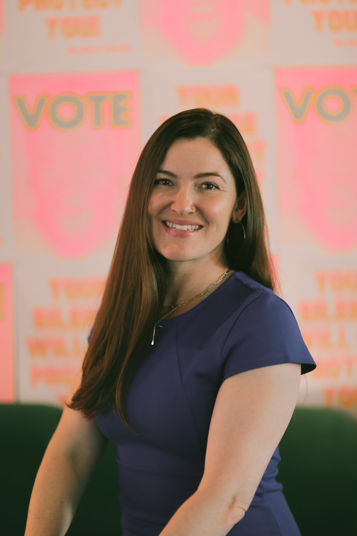 Eve is pictured from the waist up wearing a navy blouse against a pink backdrop that says "vote."
