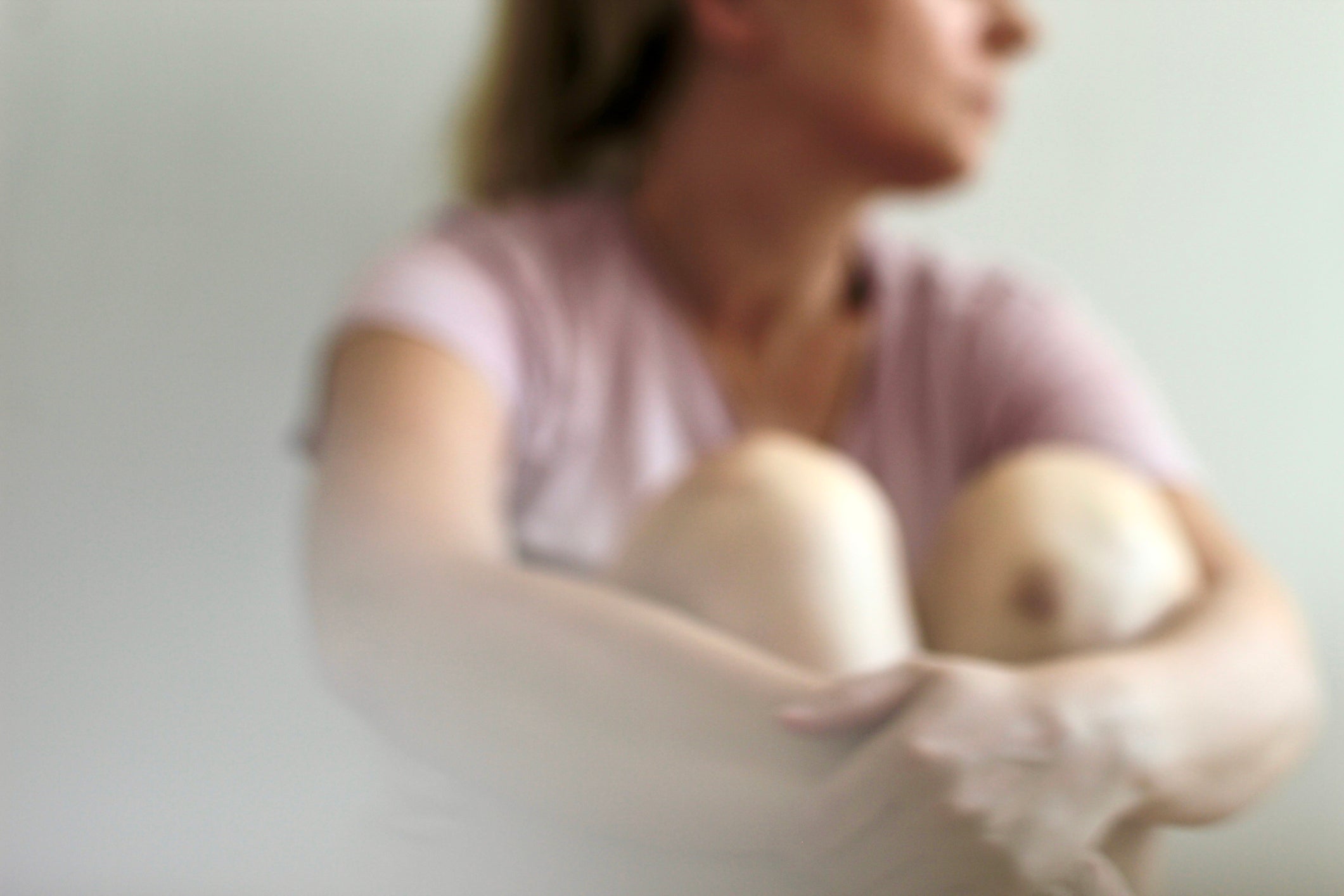 Blurred background, a woman sits with her arms around her legs and looks out the window