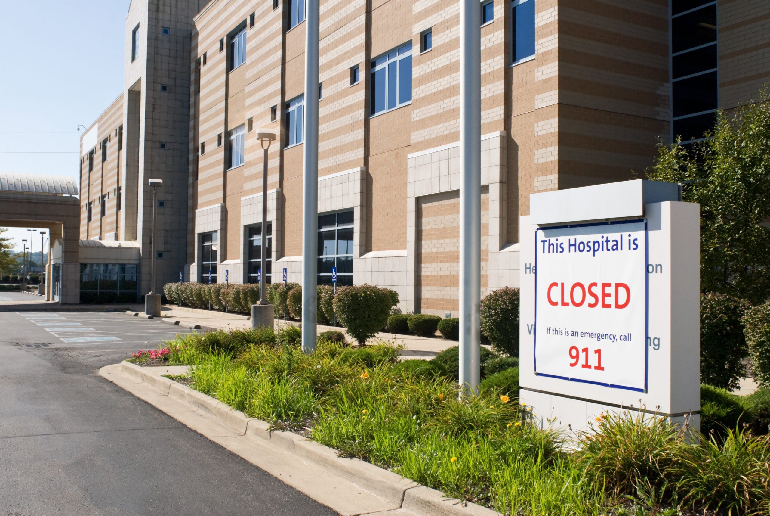 a sign reads "this hospital is closed" in front of a brick hospital building